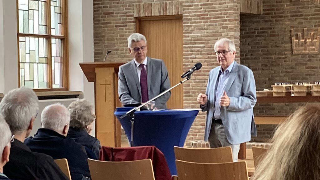 zwei personen stehen am mikrofon vor den zuhörern in der gemeinde